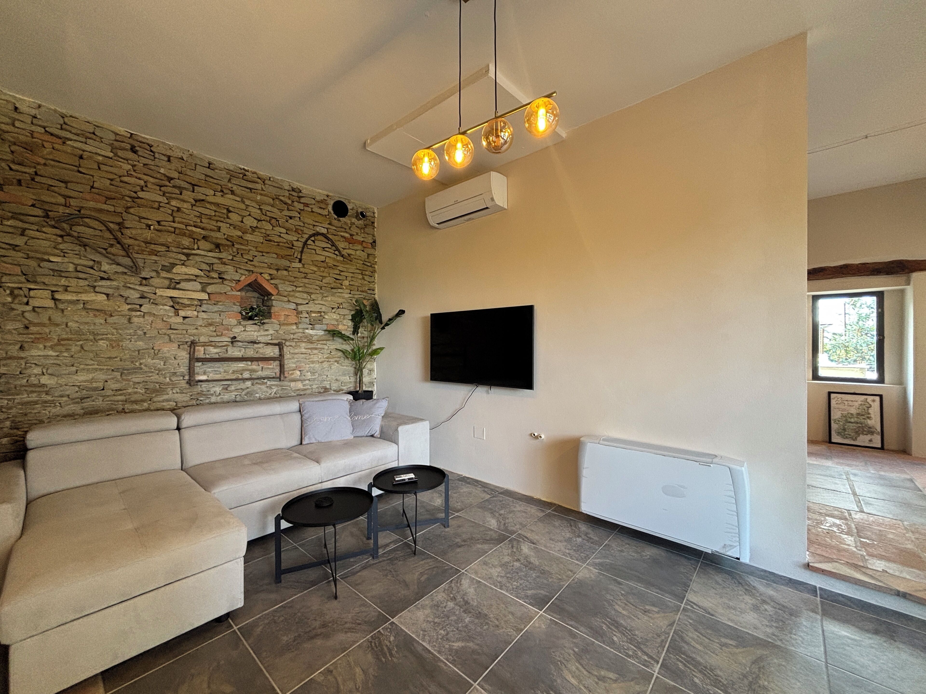 A modern living room with a stone wall, a sofa, two small tables, a mounted TV, and a radiator.