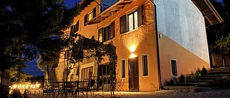 Un edificio de varios pisos con techo inclinado, zona de estar al aire libre y una entrada bien iluminada.