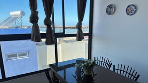 Een kamer met uitzicht op zee, een tafel met stoelen, een potplant en twee decoratieve borden aan de muur.