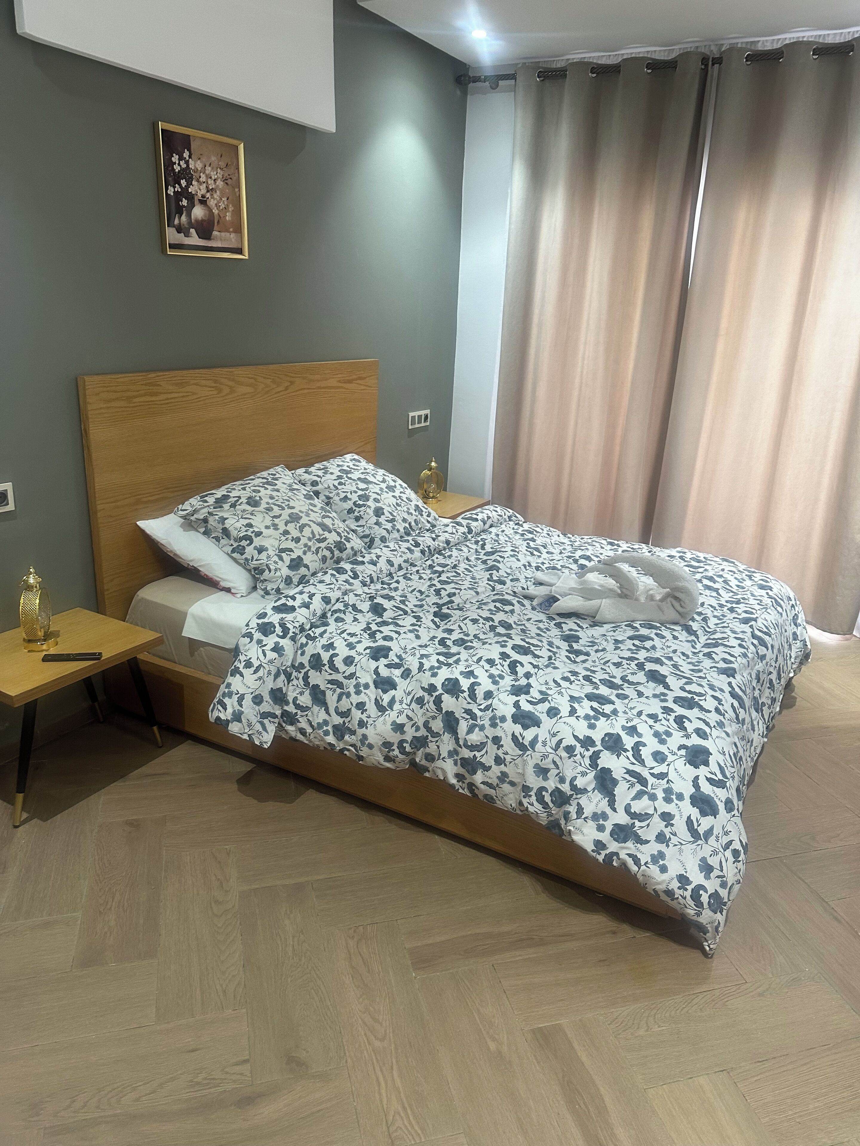 A neatly made bed with a floral bedspread, a bedside table with a lamp, and a framed picture on the wall.