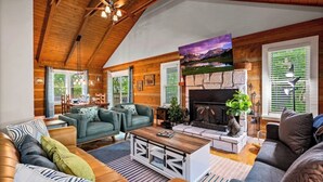 Un salon spacieux doté d’une cheminée, d’un plafond en bois et de grandes fenêtres.
