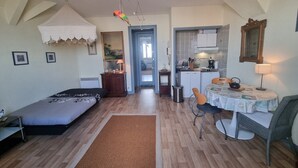 A compact living space with a bed, a small dining table, a kitchen area, and a doorway leading to another room. - Comfortable studio in the heart of Arcachon (Arcachon)