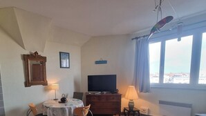 A cozy living room with a TV, wooden furniture, a dining table, and a view through a large window. - Comfortable studio in the heart of Arcachon (Arcachon)