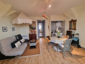 Un salon comprenant un canapé, une table basse, une table à manger avec des chaises, un coin cuisine et un miroir au mur.
