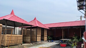 Um pátio com uma construção de telhado vermelho, cercas de bambu e um canteiro elevado.