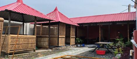 A courtyard with a red-roofed structure, bamboo fencing, and a raised garden bed.