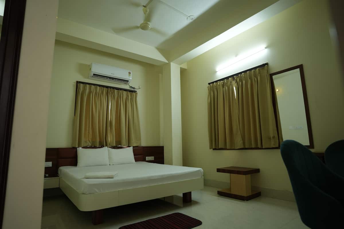 A hotel room with a bed, bedside table, chair, air conditioning unit, curtains, and a mirror.