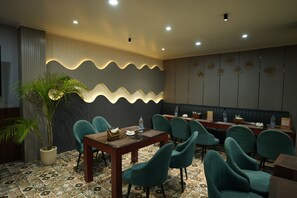 A hotel room with a dining area featuring teal chairs, a wooden table, and a decorative wall with a wavy pattern. - Hotel Royal Paradise (Islampur)