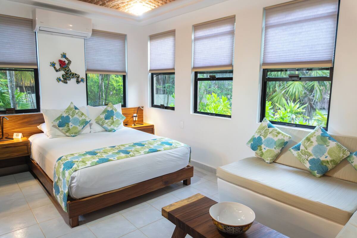 Une chambre à coucher comprenant un lit, une table de chevet en bois, une commode, un canapé et une fenêtre donnant sur un paysage verdoyant.