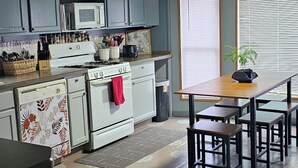 Cozinha equipada com fogão, micro-ondas e armários. Há uma mesa de jantar com cadeiras e um vaso de planta.