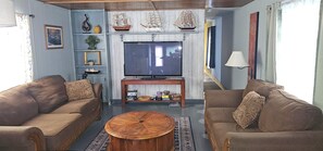 A living room with two sofas, a coffee table, a TV, and decorative items like model ships and a framed picture.