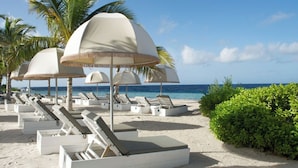 A beach with white lounge chairs and thatched umbrellas, palm trees, and a clear view of the ocean. - Apartment Casa Sweet, Jan Sofat, Pool & Tropical Garden (Willemstad)