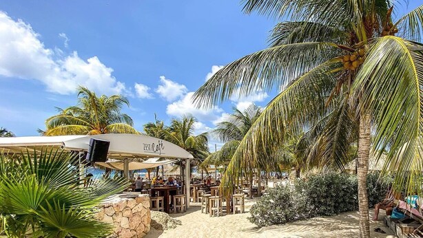 A beachside cafe with outdoor seating, palm trees, and a clear sky. - Apartment Casa Sweet, Jan Sofat, Pool & Tropical Garden (Willemstad)