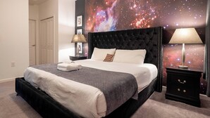 A bedroom with a bed, a nightstand, a wall mural of a galaxy, and a door. - 9BR Pool Home/ Game Room/ Theater Near Disney (Kissimmee)