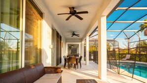 A covered patio with a pool, outdoor furniture, ceiling fans, and a dining area. - 9BR Pool Home/ Game Room/ Theater Near Disney (Kissimmee)