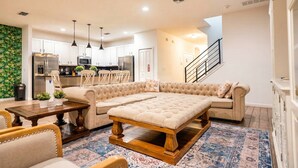 A modern living room with a sectional sofa, a wooden coffee table, and a dining area with chairs. - 9BR Pool Home/ Game Room/ Theater Near Disney (Kissimmee)
