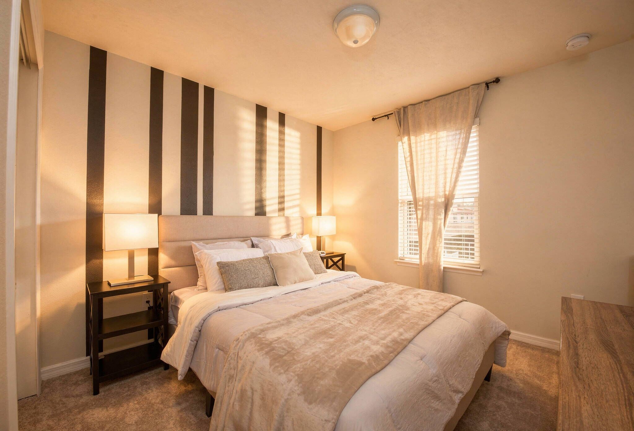 Een slaapkamer met een bed, nachtkastjes, een lamp, een raam met zonwering en een plafondlamp.