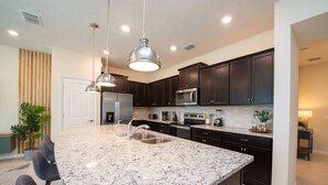 A modern kitchen with dark cabinets, granite countertops, stainless steel appliances, and pendant lighting. - 5BR Home with Private Pool Near Disney (Davenport)