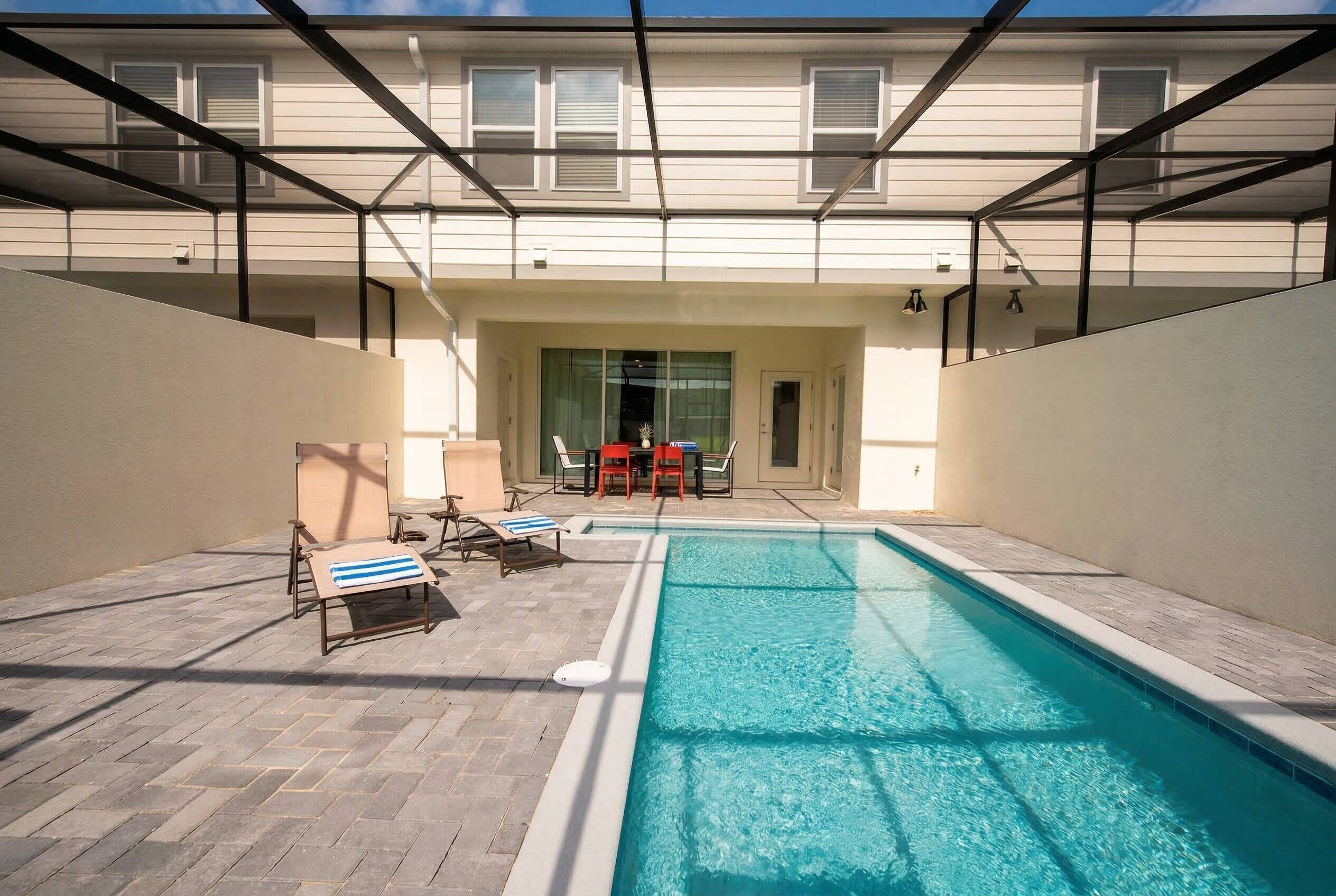 A swimming pool with lounge chairs and a table, surrounded by a covered patio area.