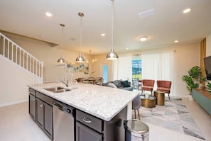 A kitchen with a granite countertop, stainless steel appliances, pendant lighting, and a dining area with a table and chairs. - 5BR Home with Private Pool Near Disney (Davenport)