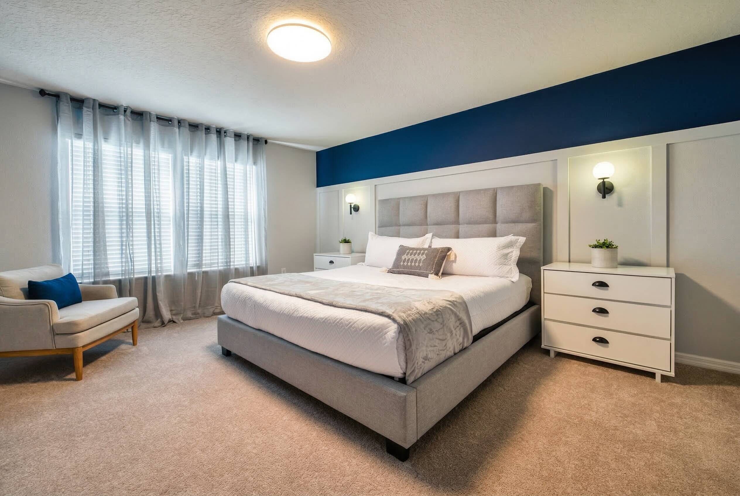 Une chambre à coucher avec un lit, une table de chevet, une chaise et une fenêtre avec des rideaux.