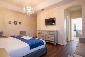 A bedroom with a large bed, a dresser, a TV, and a chandelier. - 6BR Family Home w/ Pool Near Disney (Kissimmee)