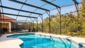 A swimming pool with a glass enclosure, surrounded by a patio area with chairs. - 6BR Family Home w/ Pool Near Disney (Kissimmee)