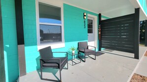 A modern outdoor seating area with two chairs and a small table, a large window, and a door with the number 1633.