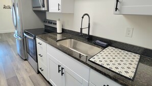 A modern kitchen with white cabinets, a stainless steel refrigerator, a microwave, and a sink with a patterned backsplash.
