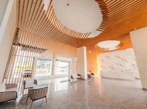 Um lobby moderno com teto de ripas de madeira, balcão de recepção e áreas de estar.