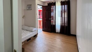 Ein Zimmer mit Holzboden, einem Bett, einem Deckenventilator und einer Tür zu einem weiteren Raum.