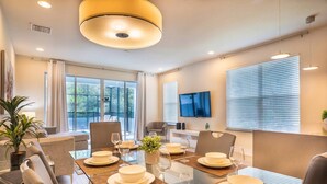 Une salle à manger moderne avec une table en verre, des chaises et une grande fenêtre équipée de stores.