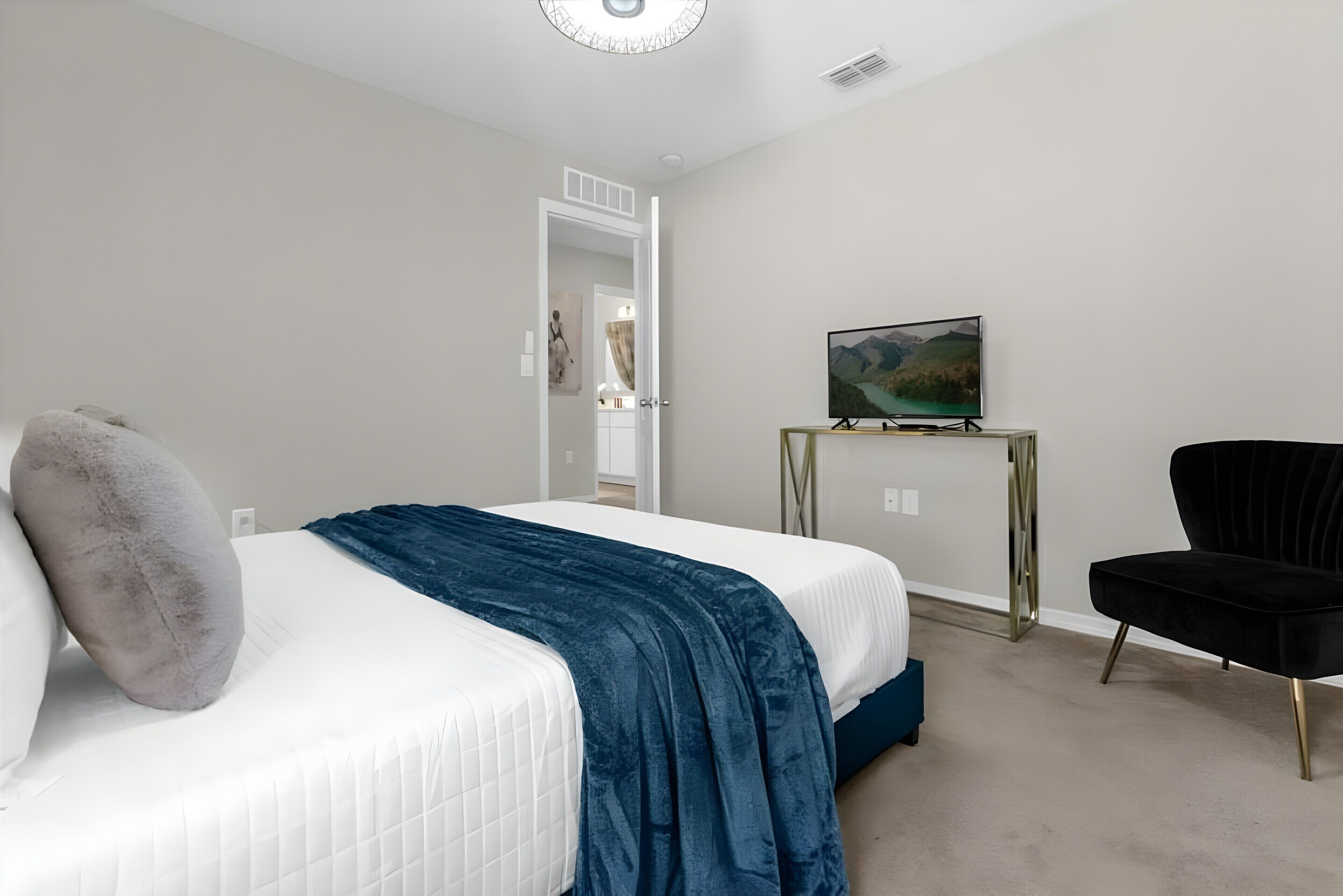 Una camera da letto con un letto, una TV su un mobile, una sedia nera e una porta che dà su un'altra stanza.