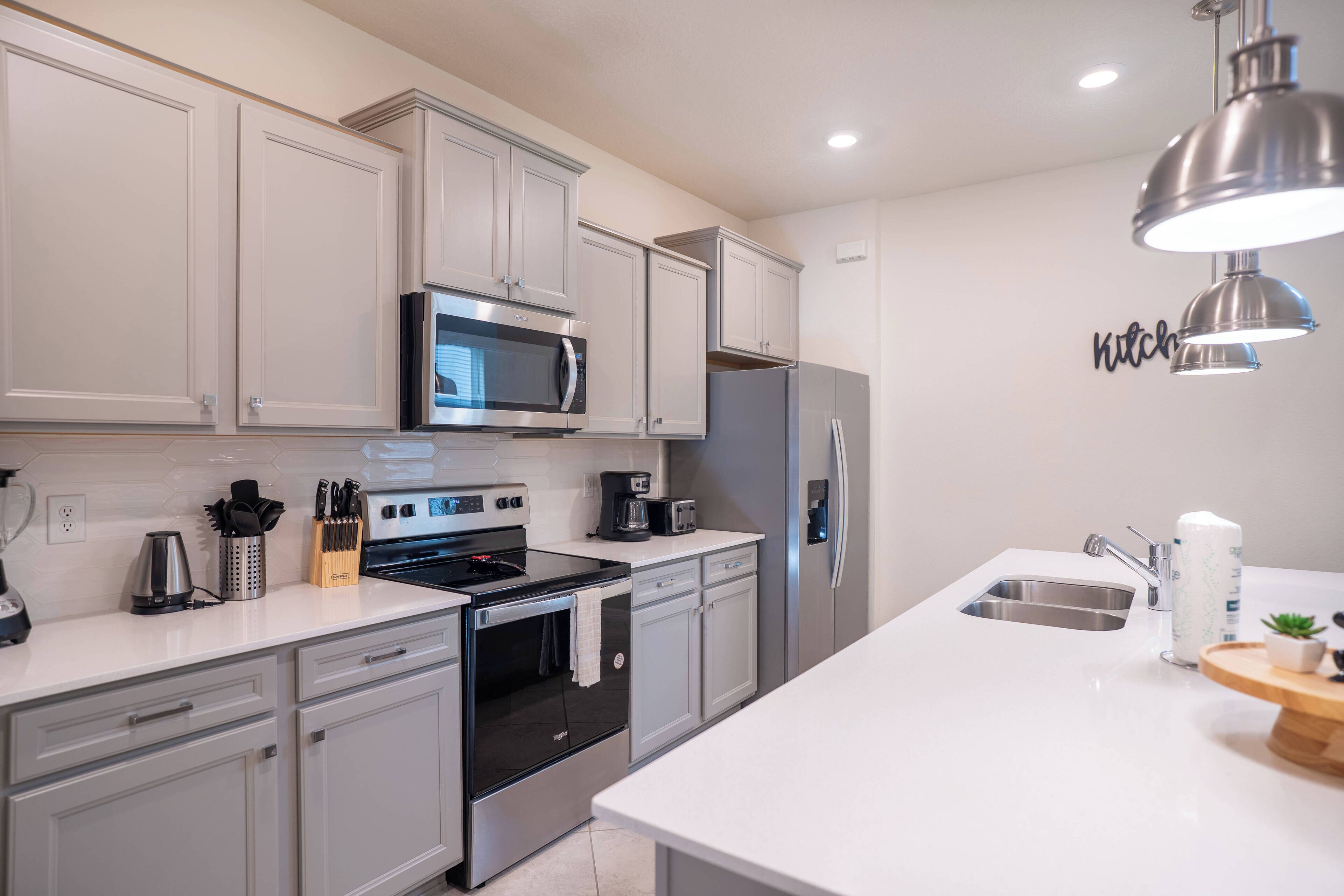 This contemporary kitchen boasts sleek gray cabinetry and a spacious white countertop ideal for meal prep or a casual breakfast. Stylish stainless steel appliances and modern pendant lighting enhance its functionality and charm.