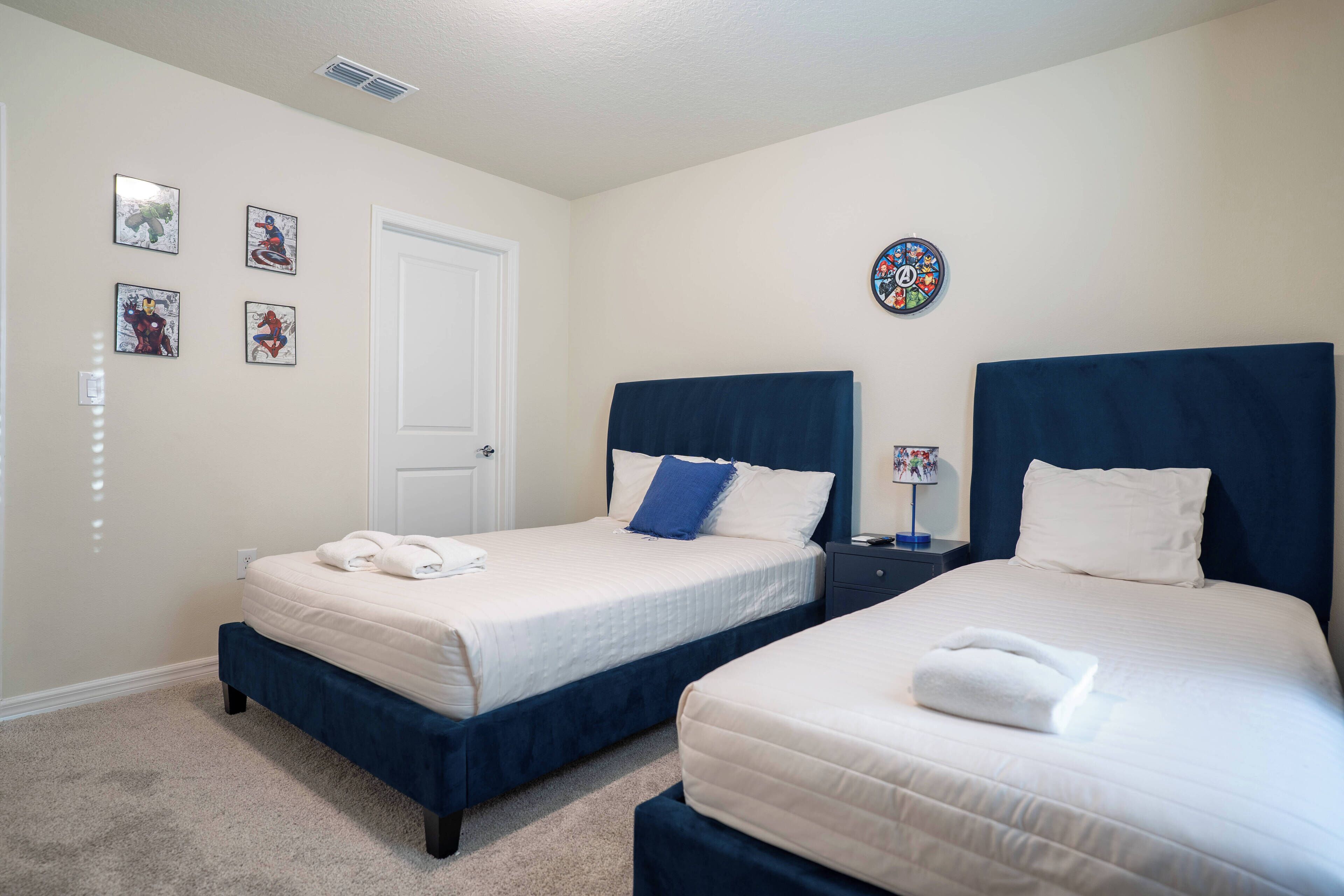 A hotel room with two beds, a door, and four framed pictures on the wall.