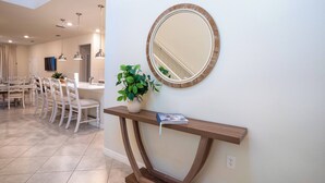 A modern kitchen with white chairs, a wooden console table, a potted plant, and a round mirror on the wall. - 6BR Family Pool Home at Windsor Cay (Clermont)