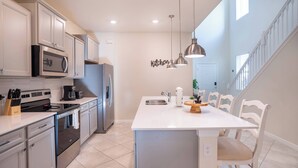 A modern kitchen with stainless steel appliances, a central island with seating, and a staircase leading to another level. - 6BR Family Pool Home at Windsor Cay (Clermont)