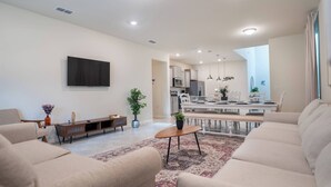 A modern living room with a flat-screen TV, beige sofas, a wooden coffee table, and a patterned rug. - 6BR Family Pool Home at Windsor Cay (Clermont)