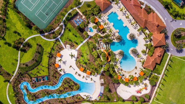 Luchtbeeld van een resort met een groot zwembad, tennisbanen en een kronkelende waterglijbaan.