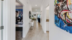 A hallway with a bed, a table with a vase, and a large abstract painting on the wall. - Family 5BR Retreat Near Disney (Kissimmee)