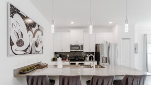 A modern kitchen with white cabinets, stainless steel appliances, and a large island with bar stools. - Family 5BR Retreat Near Disney (Kissimmee)