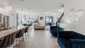 A modern kitchen with a large island, dining area with chairs, a sofa, and a staircase leading to another level. - Family 5BR Retreat Near Disney (Kissimmee)