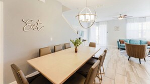 A dining area with a long table, chairs, a chandelier, and a wall-mounted sign. - Storey Lake 5BR Family Home w/ Private Pool (Kissimmee)