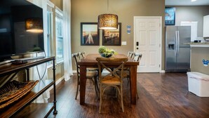 A dining area with a wooden table, chairs, a television on a stand, a hanging light fixture, and a refrigerator in the background. - Home in West Lucaya | 4BR Near Disney (Kissimmee)