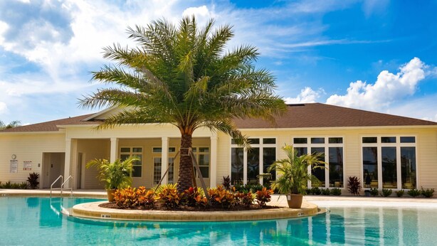 A swimming pool with a palm tree, a building with large windows, and a clear sky. - Home in West Lucaya | 4BR Near Disney (Kissimmee)