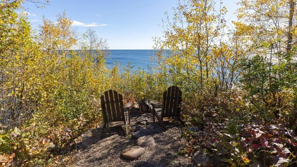 Zwei Adirondack-Stühle mit Blick auf ein Gewässer, umgeben von Herbstlaub.
