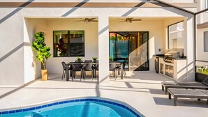 A modern outdoor patio with a pool, seating area, and a barbecue setup. - Luxury 12BR Home w/ Pool & Game Room (Orlando)