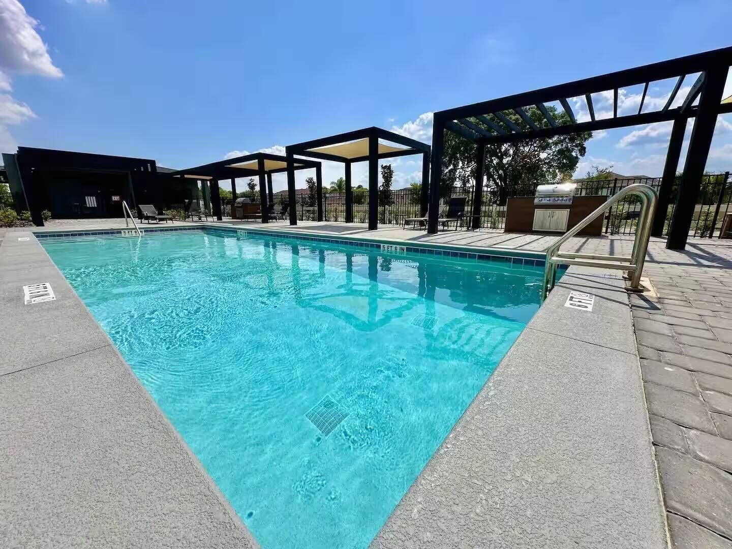 Una piscina rectangular con agua azul cristalina, rodeada por un solárium con baldosas y zonas con sombra.