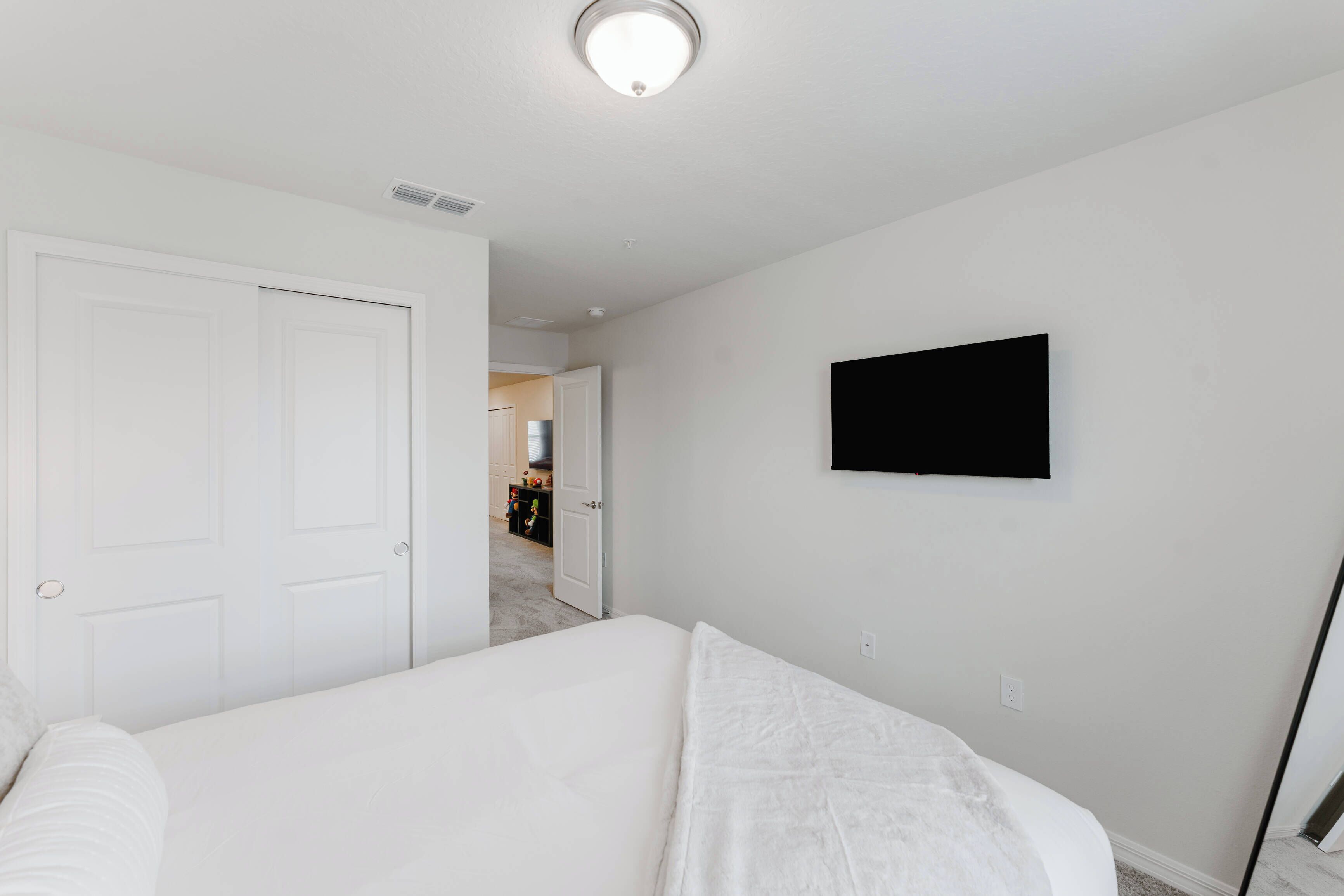 Un dormitorio con cama, una puerta blanca y televisor montado en la pared.