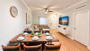 A dining area with a wooden table set for four, a ceiling fan, and a television on the wall. - Renovated 3BR Home | Mickey Room | Near Disney (Kissimmee)